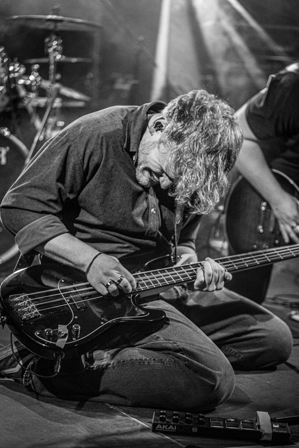 Schwarzweiß: Bassist kniet auf der Bühne